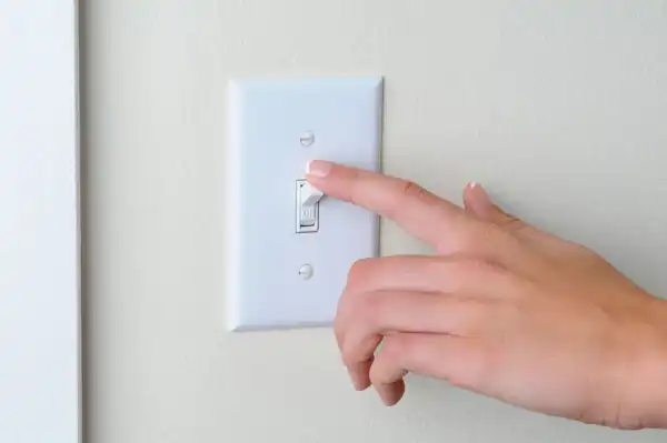 closeup of a person's hand going to turn off a light switch on a light yellow wall