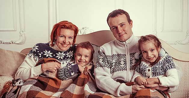 Family sitting on couch smiling at the camera in holiday sweaters