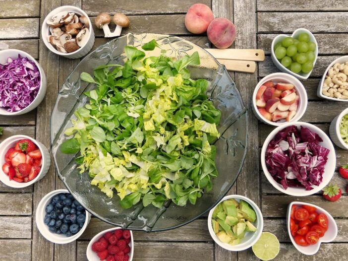 a big salad surrounded by smaller bowls with fruits and vegetables