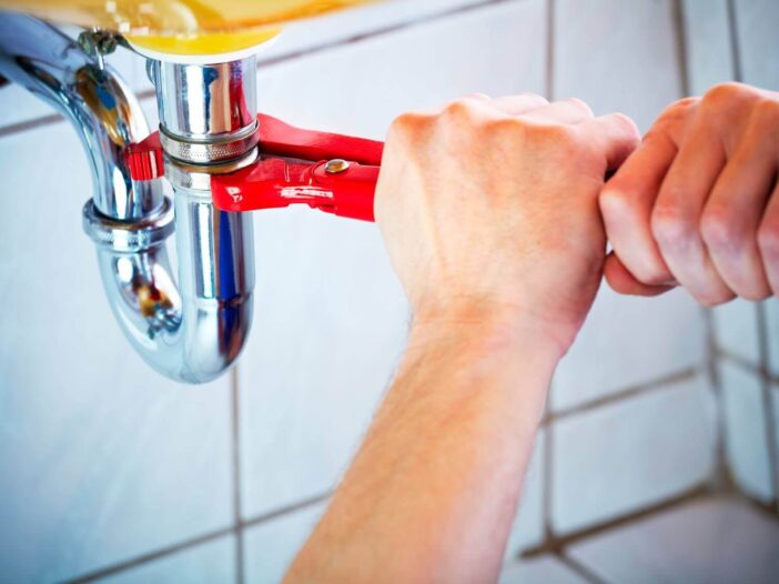 Closeup of someone adjusting pipes with a wrench under a sink