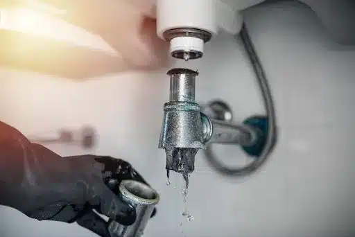 A close-up of a plumber's hand using taking apart the pipes of a sink to locate a clog in the home of a Mission, KS resident.