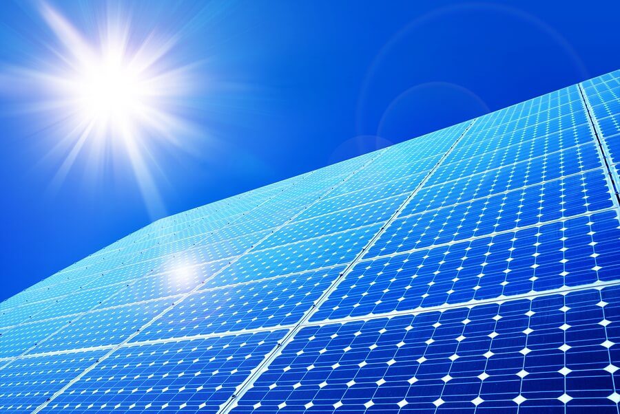 Bright sunlight shines on a large array of blue solar panels, capturing renewable energy under a clear blue sky.