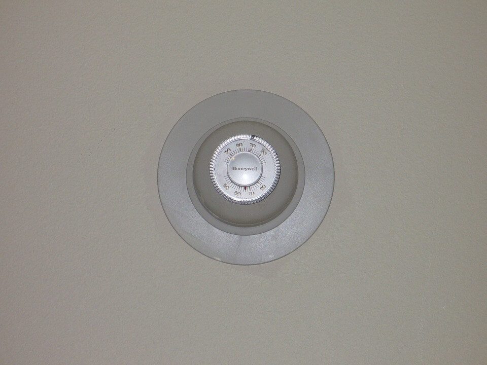 A round thermostat on a beige wall, displaying temperature settings in a simple, circular design.